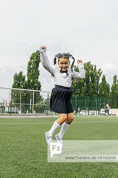 Carefree girl wearing uniform jumping in school lawn
