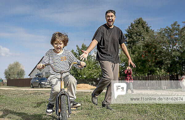 Happy father looking at son riding bicycle on sunny day