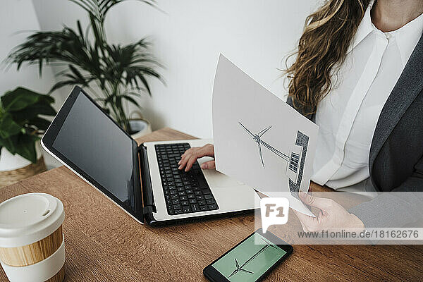 Junge Geschäftsfrau arbeitet in einem modernen Büro und hält den Plan einer Windkraftanlage in der Hand