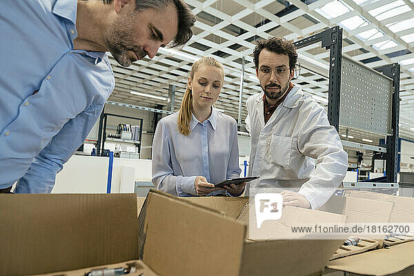 Ingenieur steht einem Geschäftsmann und einer Geschäftsfrau zur Seite und untersucht die Ausrüstung im Karton in der Fabrik
