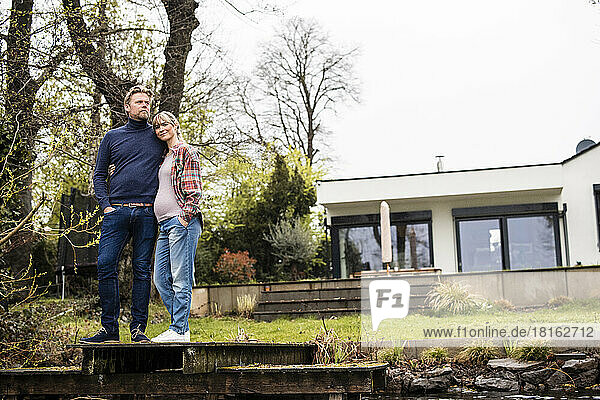 Expectant couple standing on jetty in front of house