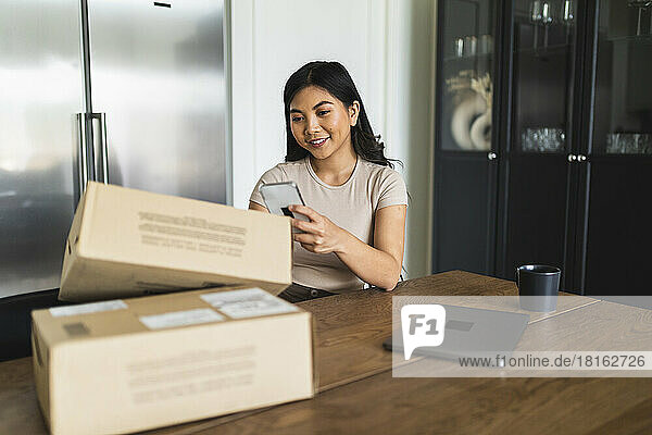 Smiling woman checking home delivery box at dining table