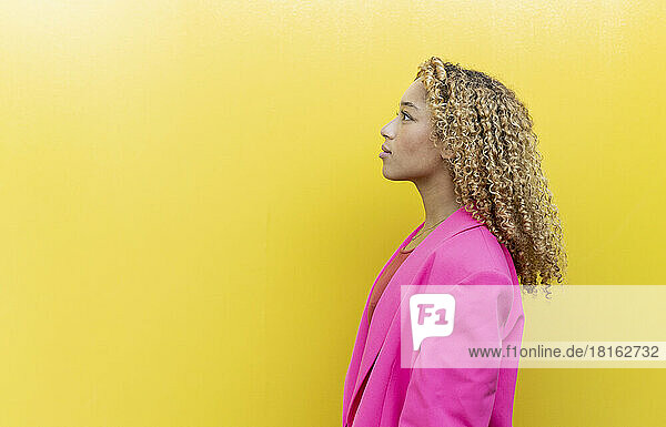 Young woman contemplating by yellow background