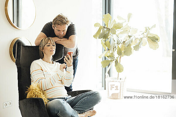 Pregnant woman sitting on chair sharing smart phone with man at home