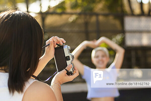 Young woman photographing friend through camera on sunny day