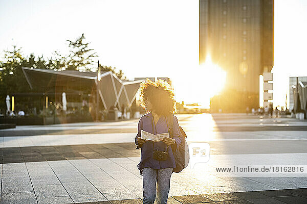 Afro woman holding map walking on footpath