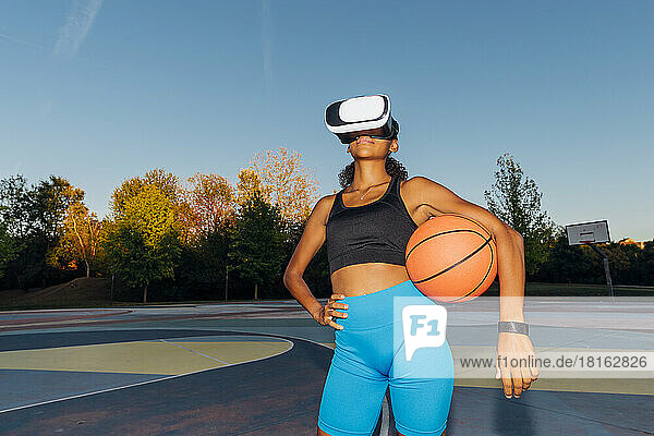 Young basketball player with ball and VR Goggles at sunset