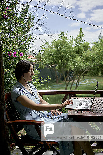 Freelancer using laptop sitting on chair on balcony