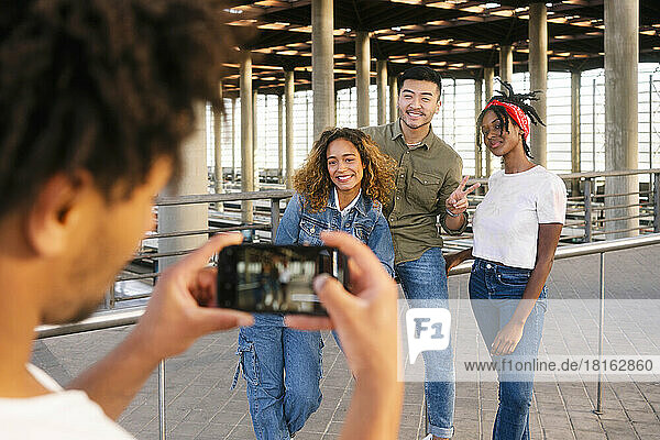 Man photographing multiracial friends posing at railroad station
