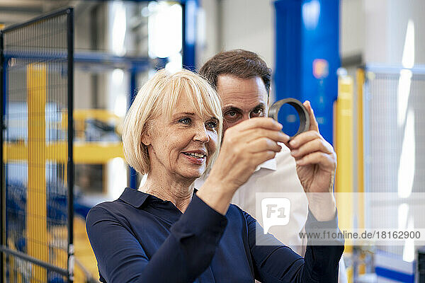 Smiling senior businesswoman with businessman analyzing machine part in industry