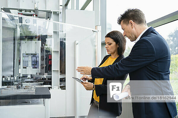Businesswoman and businessman discussing over tablet PC in industry