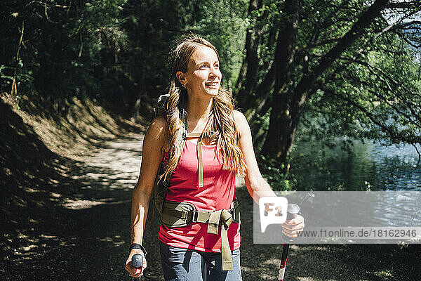 Smiling woman hiking by lake on sunny day