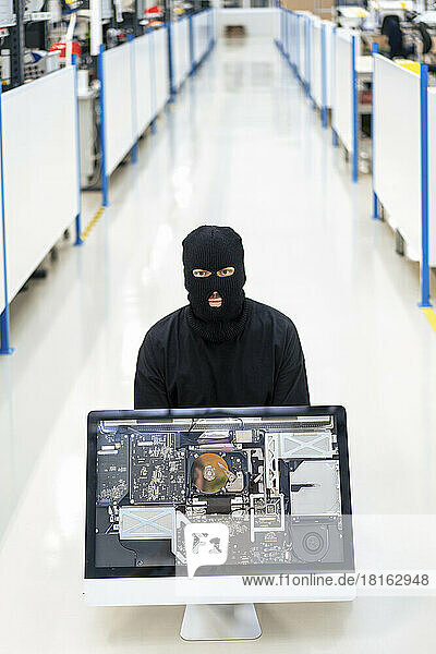 Dieb mit Maske sitzt mit Desktop-PC auf dem Boden in der Industrie