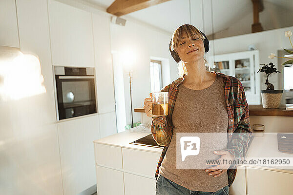 Pregnant woman touching belly listening to music through headphones at home