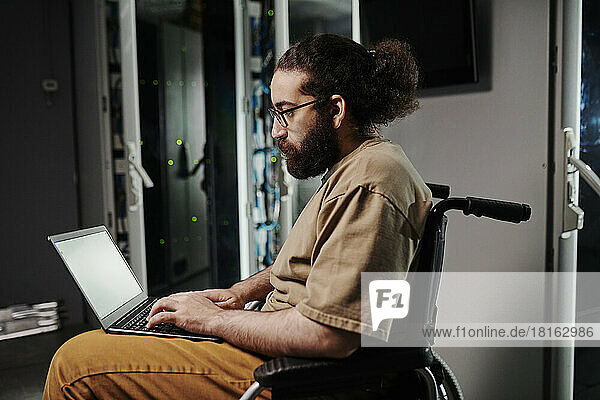 IT expert sitting on wheelchair using laptop in server room