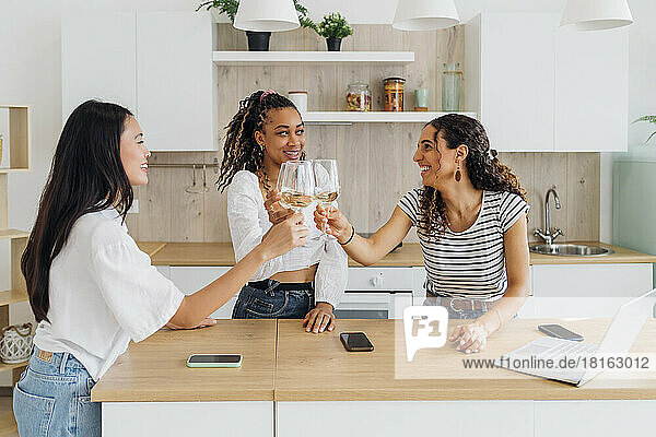 Happy roommates toasting wineglasses in kitchen at home