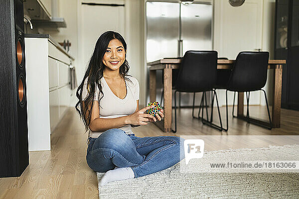 Happy woman with puzzle cube sitting on carpet at home