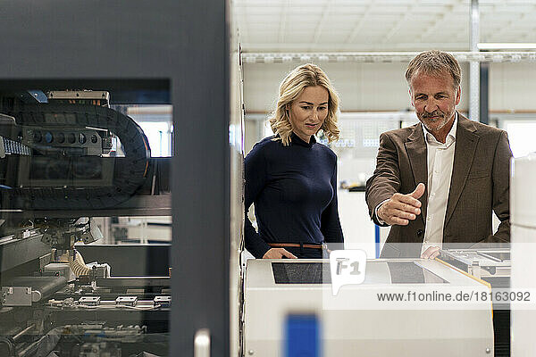 Businesswoman with colleague discussing over machine in industry