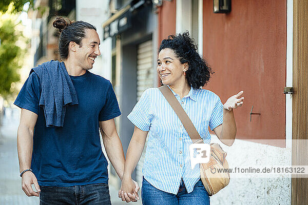 Smiling woman gesturing and talking to boyfriend by building