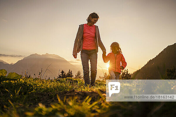 Smiling woman holding daughter's hand walking on mountain