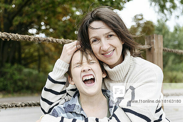 Lächelnde Mutter umarmt schreienden Sohn im Park