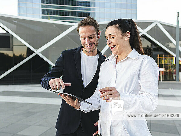 Cheerful businesswoman with colleague using tablet PC standing at office park