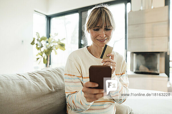 Smiling woman doing online shopping through credit card at home