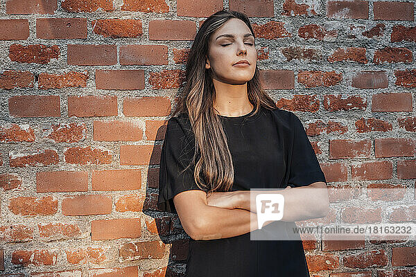 Young woman with eyes closed standing in front of brick wall