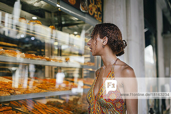 Young woman looking through delicatessen store window