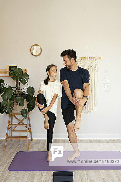 Smiling man with daughter doing yoga on exercise mat at home