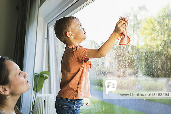 Son helping mother to clean window at home