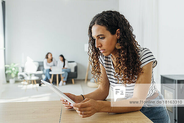 Young woman leaning on table using tablet PC in living room at home