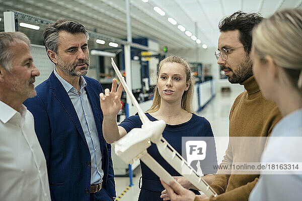 Young businessman discussing over wind turbine model with colleagues in industry