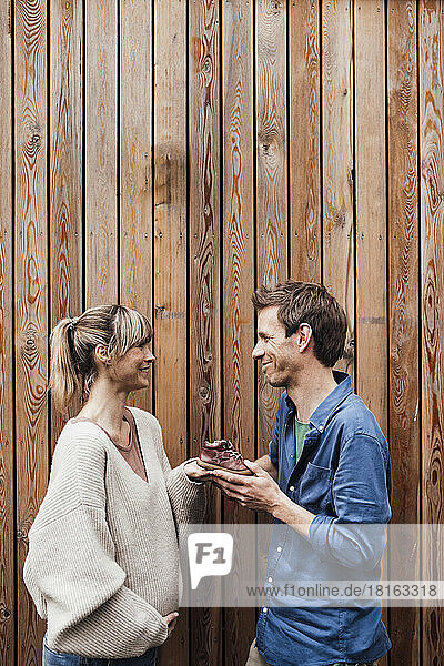 Pregnant woman holding baby booties with man in front of wooden wall