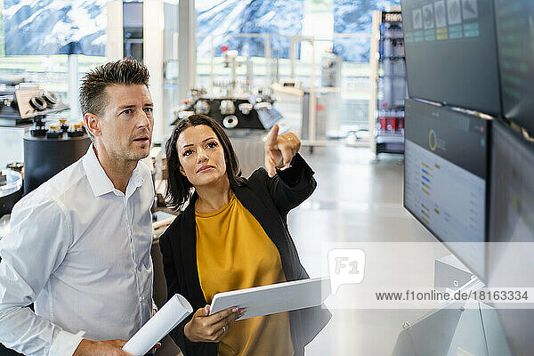 Businesswoman holding tablet PC gesturing by standing businessman