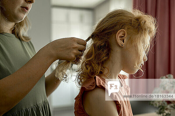 Mother braiding hair of daughter at home
