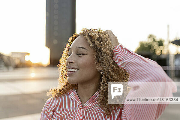 Smiling young woman with hand in hair and eyes closed at sunset
