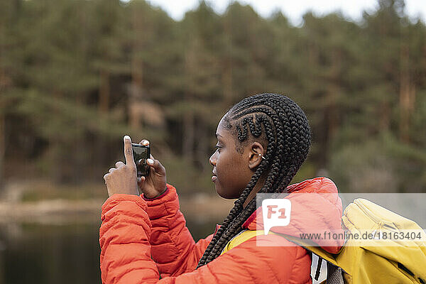 Young woman with braided hair photographing with smart phone