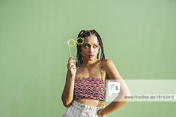 Young woman holding eyeglasses prop in front of green wall