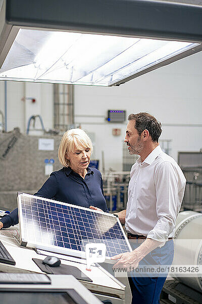 Businessman holding solar panel discussing with businesswoman in industry