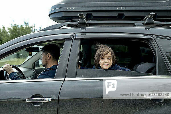 Cute boy looking out of window with father driving car