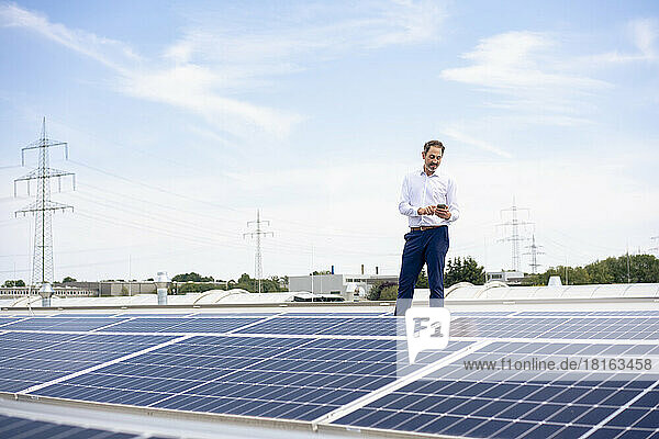 Businessman using smart phone standing by solar panels on rooftop