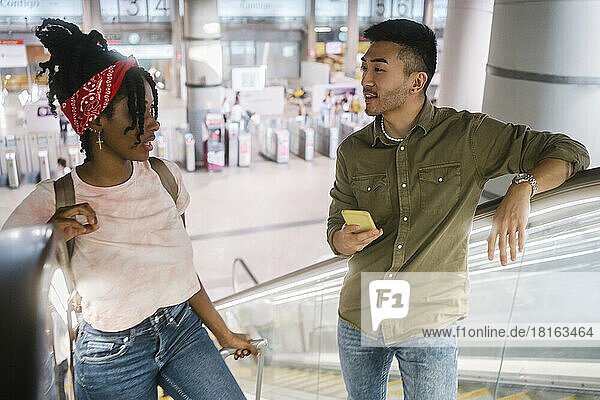Young man and woman talking on escalator at railroad station