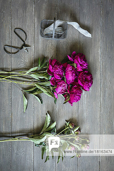Scissors  ribbon and freshly cut peonies lying on wooden surface