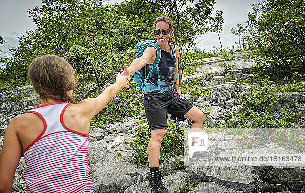 Happy woman holding daughter's hand climbing mountain