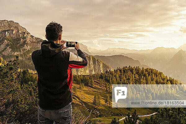 Man photographing mountain through smart phone at sunset
