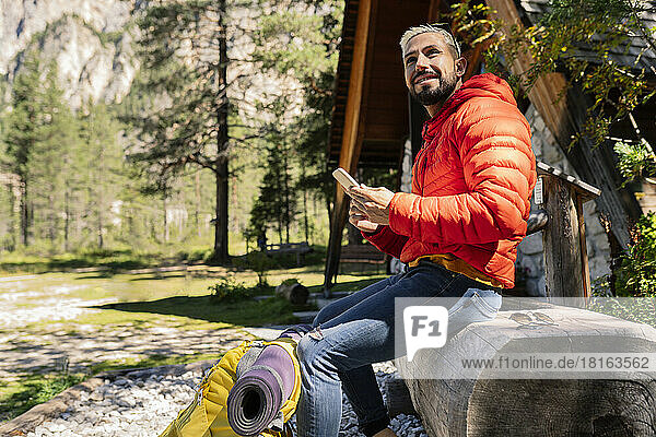 Smiling hiker with smart phone sitting on drinking fountain