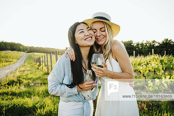Happy friends holding glass of wine embracing at winery