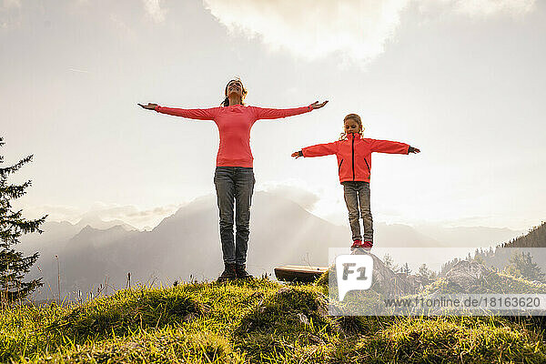 Smiling woman and daughter standing with arms outstretched