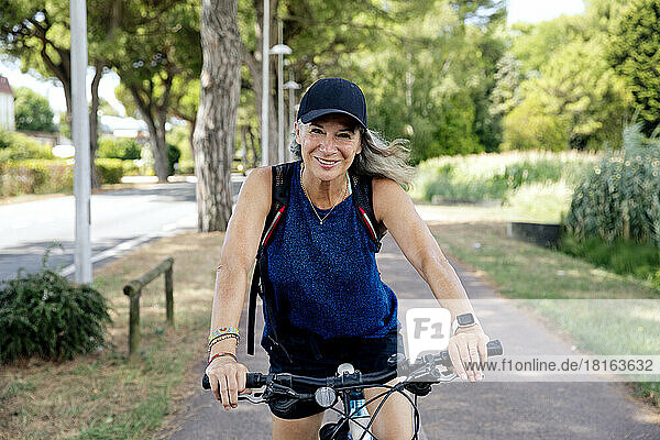 Smiling senior woman with bicycle on footpath